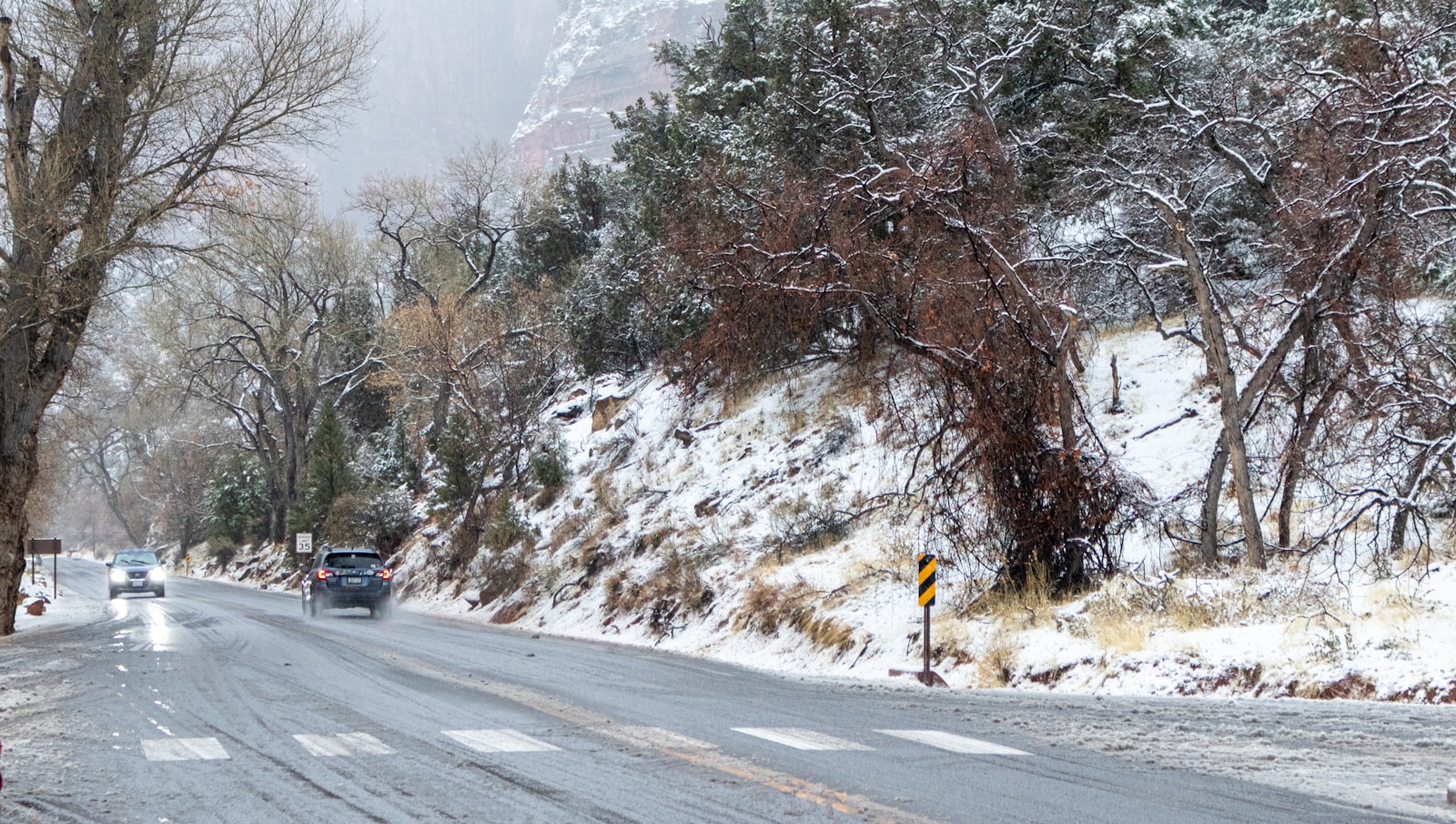Cars driving on a wet road during a snowstorm.